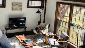 Kodikas olohuone, jossa on televisio, mukavat istuimet, sohvapöytä ja suuret ikkunat, joista avautuu näkymä ulos.