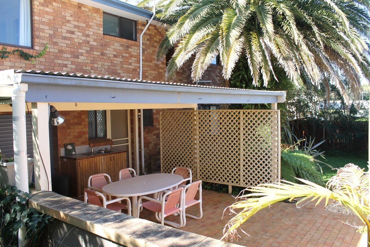 A patio with a brick wall, a wooden table with chairs, and a white fence.