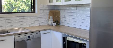 Una cocina moderna con armarios blancos, lavavajillas, microondas y refrigerador.