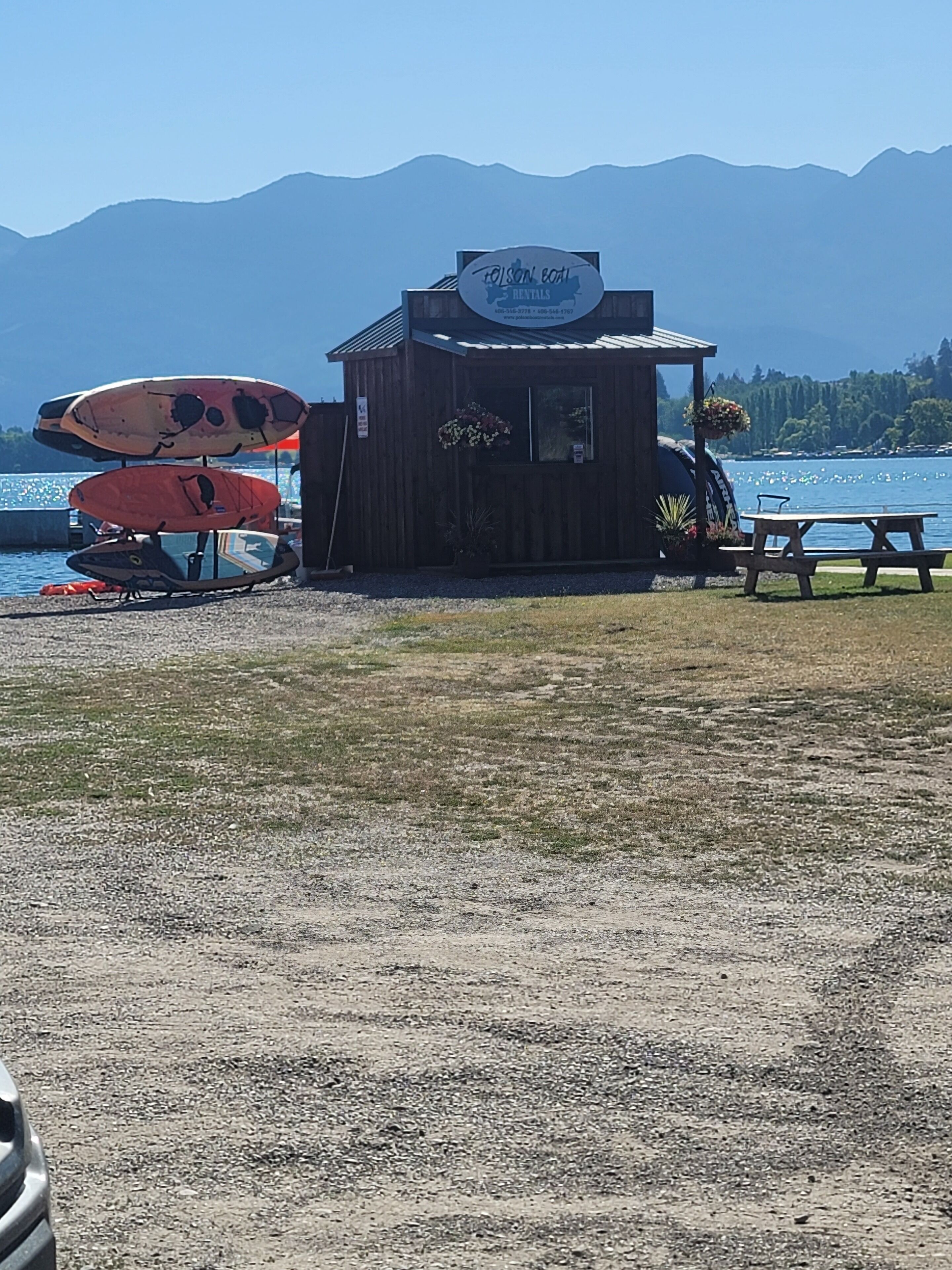 A small wooden building with a sign for 'Toison Bay Rentals' near a body of water with kayaks.