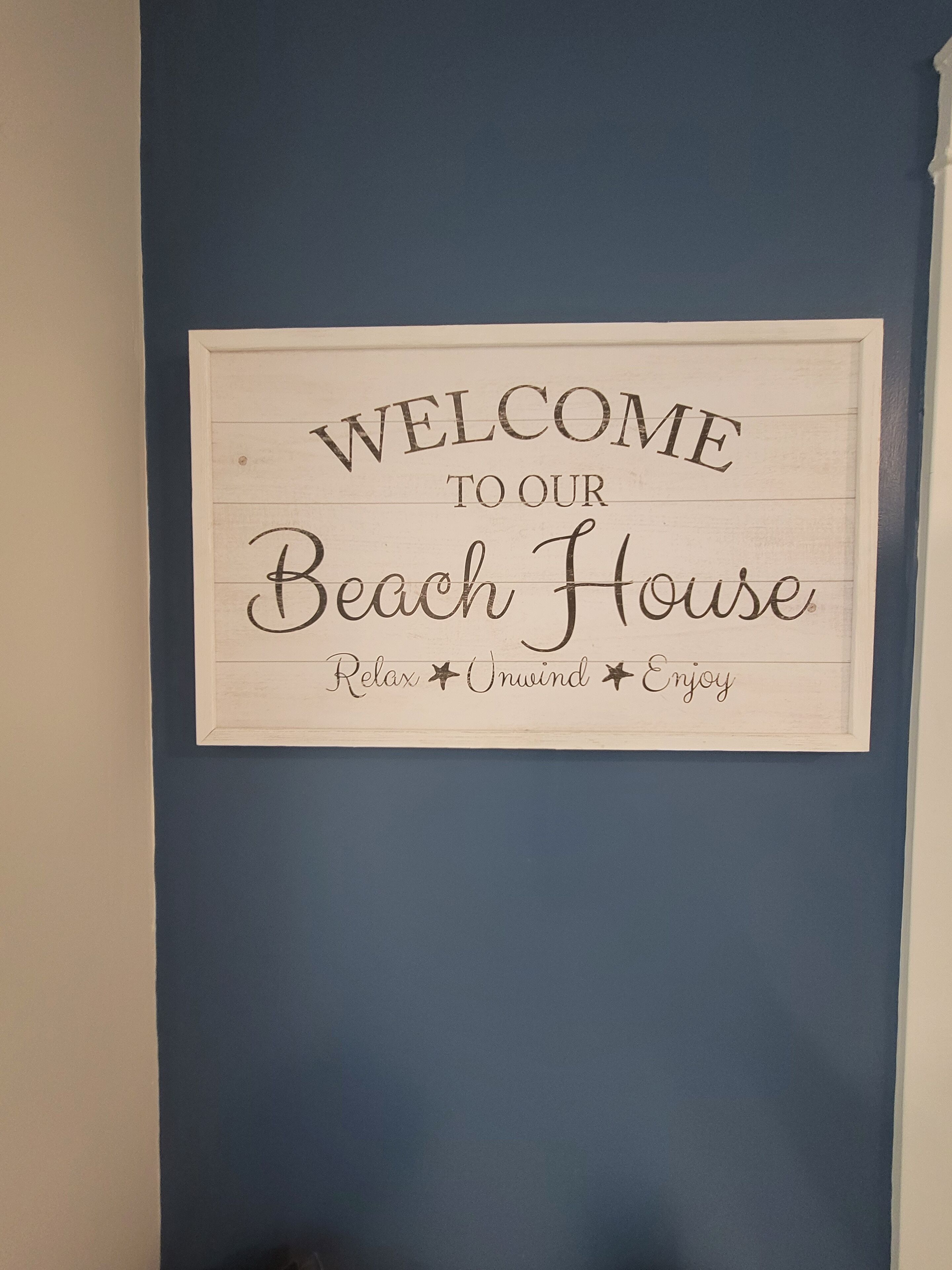 A welcome sign for a beach house with the words "Welcome to our Beach House" and the phrases "Relax," "Unwind," and "Enjoy."