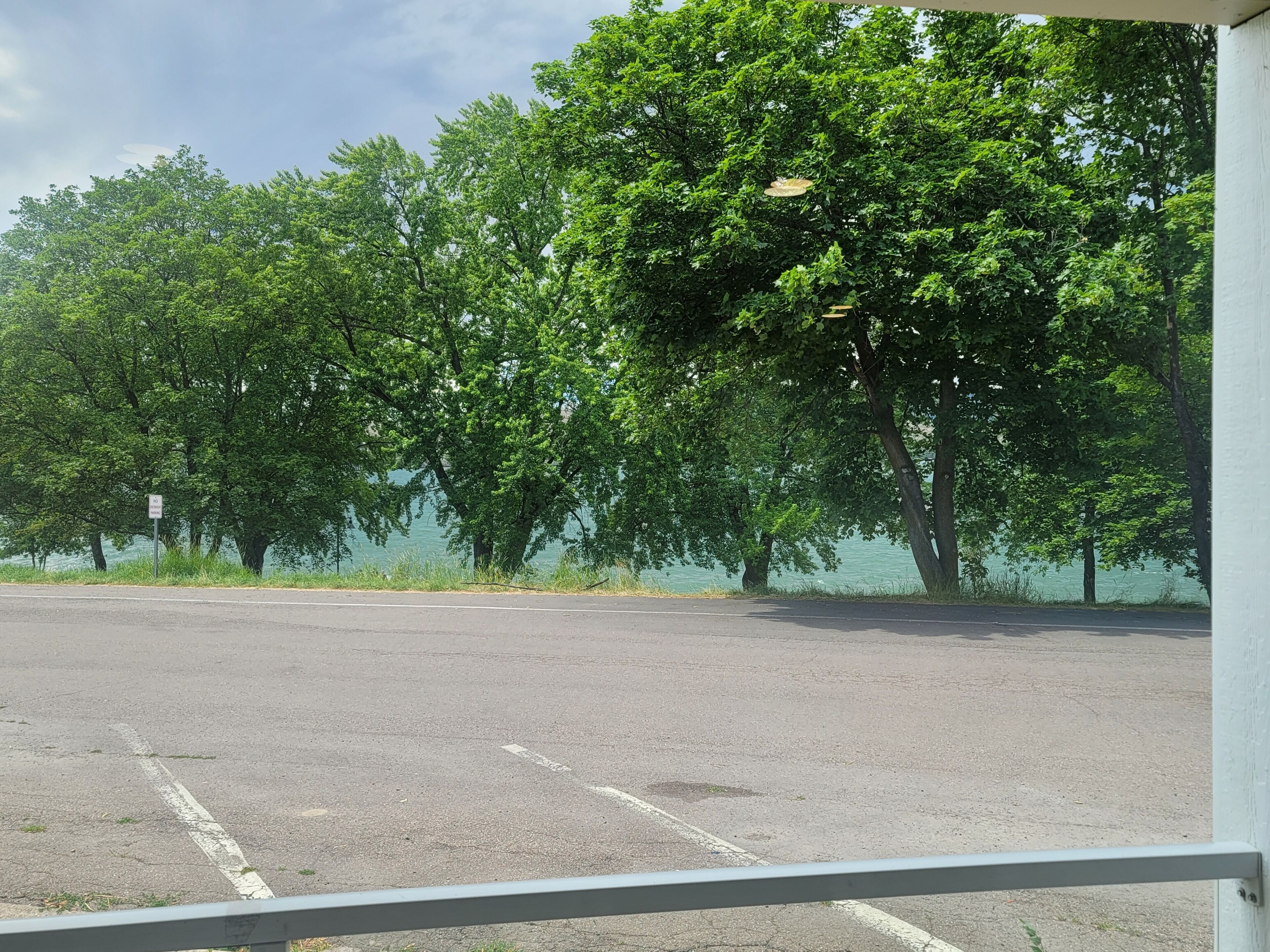 Een parkeerplaats met bomen en een waterpartij op de achtergrond.