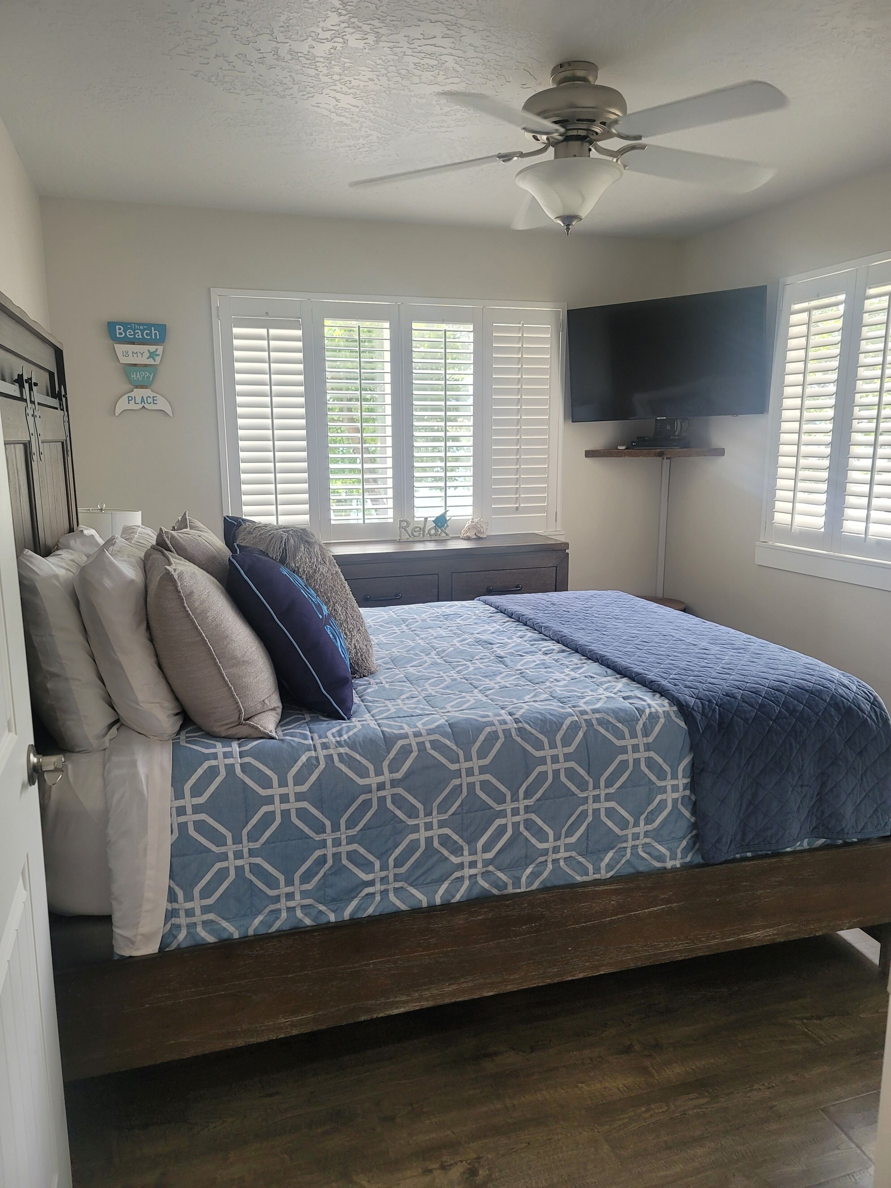 Quarto com cama, ventilador de teto, televisão e janela com persianas.