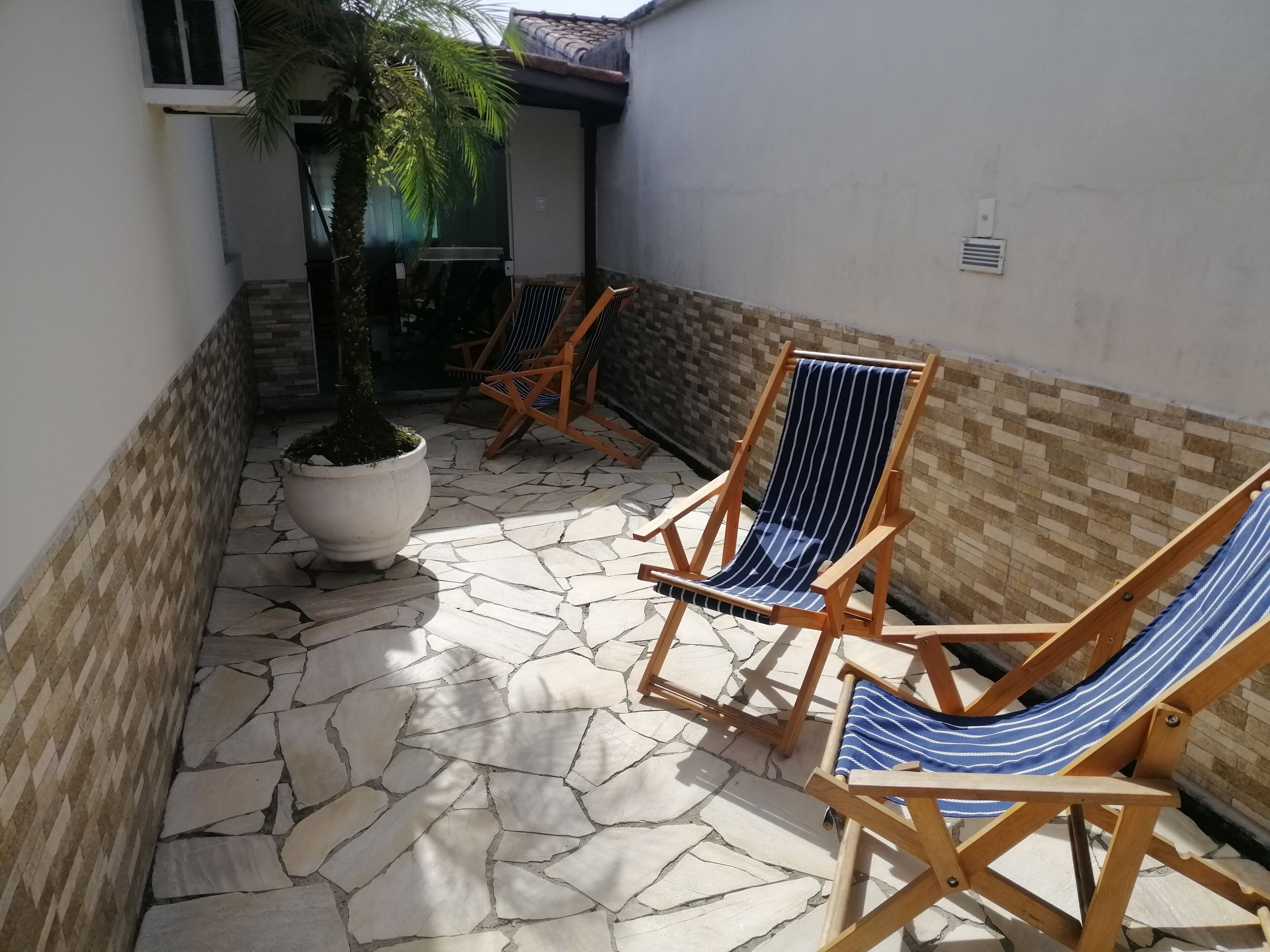 Un patio con piso de piedra, dos sillones de madera y una planta grande en maceta.