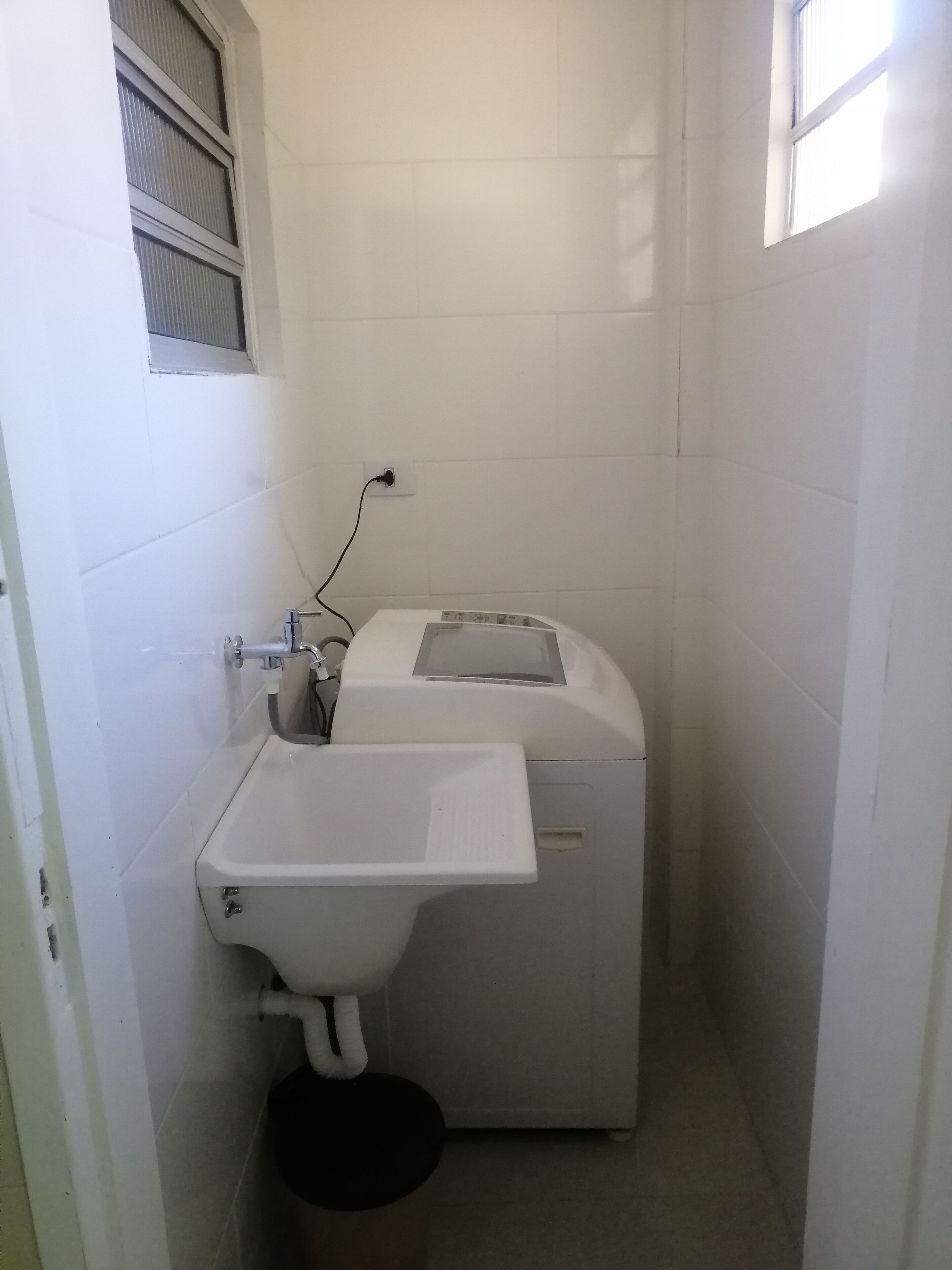 Une petite salle de bain aux murs blancs, avec un lavabo blanc, un lave-linge et une fenêtre.