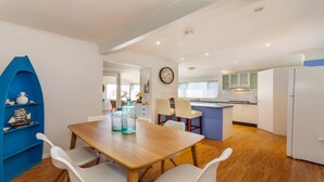 Een moderne keuken met witte kasten, een blauw kookeiland en een houten eettafel met witte stoelen.