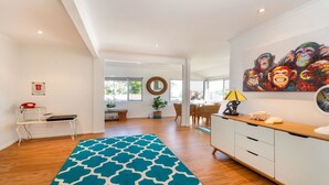 Een ruime woonkamer met een groot blauw tapijt met patroon, een eettafel met stoelen, een wit kastje en een kleurrijk schilderij aan de muur.