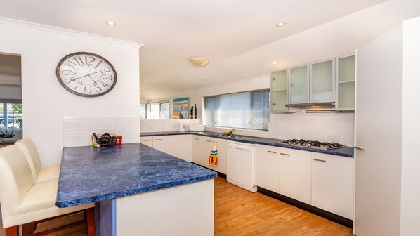 A modern kitchen with white cabinets, a blue marble countertop, and a large wall clock. - Dog Lovers Retreat - Beachmere (BEACHMERE)