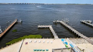 A waterfront area with a pier extending into the water, a sandy beach with lounge chairs, and a clear view of the water. - Bayfront Home with Pier, Multi-Level Decks & Stunning LBI Views (Manahawkin)