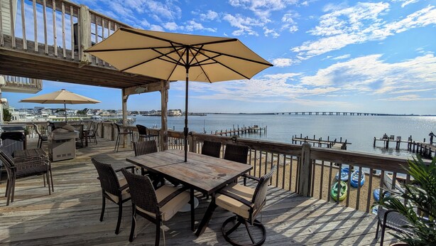 A wooden deck with outdoor seating, a table, and an umbrella. - Bayfront Home with Pier, Multi-Level Decks & Stunning LBI Views (Manahawkin)
