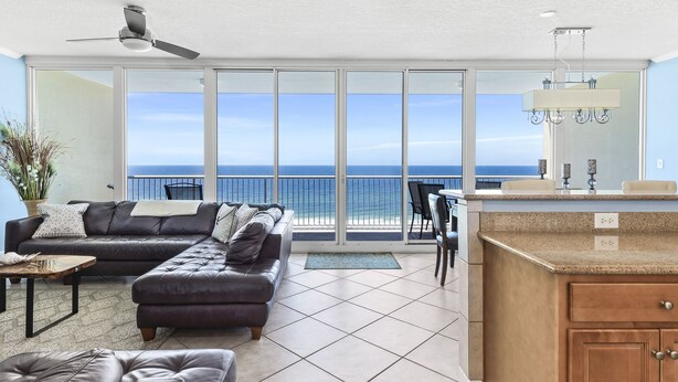 A modern living room with a large sofa, a dining area, and a kitchen with a view of the ocean.