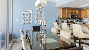 A dining area with a glass table, cushioned chairs, and a chandelier.