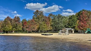 Ein Park am Seeufer mit Sandstrand, Spielgeräten und einem kleinen Gebäude, vermutlich eine Toilette oder ein Kiosk.