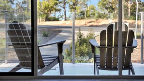 Two wooden Adirondack chairs on a balcony with a view of a road and trees. - The White House - Merimbula (Merimbula)