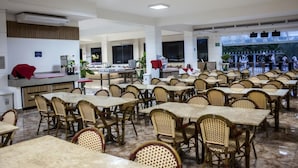 A spacious dining area with multiple tables and wicker chairs, a reception desk, and large windows offering a view of the outdoors. - Apartment in Brazil's Largest Hot Springs Resort + 12 Pools, Water Slide and Fun (Privê das Caldas)