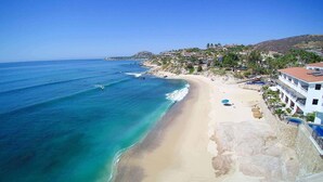 Un hôtel situé sur la côte, avec vue sur la plage, une piscine et une colline parsemée de bâtiments.