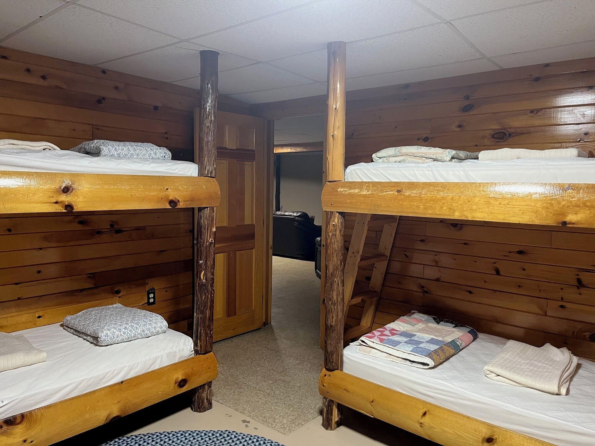 Una habitación con dos literas, paredes de madera y una puerta que da a otra estancia.