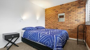 Un dormitorio con una cama, una mesita de noche, un espejo y una pared de ladrillo.