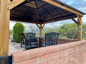 A covered patio with a brick wall, a wooden pergola, and a table with chairs. - AZ Desert Hills II Townhouse, Private with Stunning Mountain View! (Green Valley)