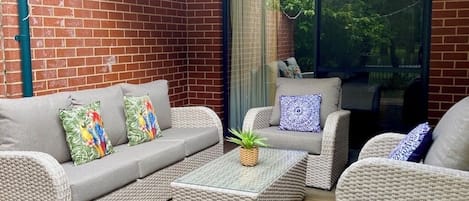 A cozy outdoor seating area with wicker furniture, a cushioned sofa, and a coffee table.