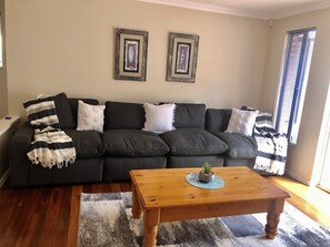 A living room with a dark grey sectional sofa, a wooden coffee table, and two framed pictures on the wall. - Salt & Peppies - across from beach, wi-fi (Dunsborough)