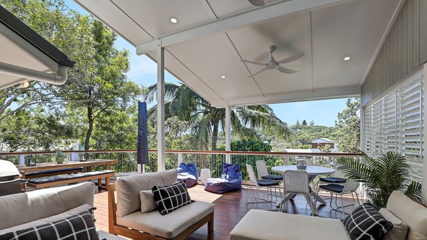 Un espace extérieur aménagé en terrasse, avec des sièges, un ventilateur de plafond et une vue sur la végétation environnante.
