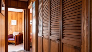A wooden hallway with a door leading to a room with a bed and a chair.