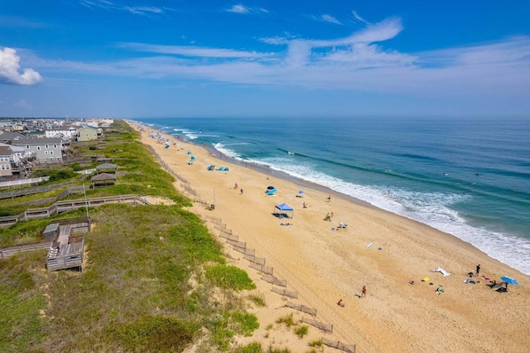 A beach with a wooden boardwalk, beach umbrellas, and people. - 320 Dog-Friendly & Across from Beach Access! (Nags Head)
