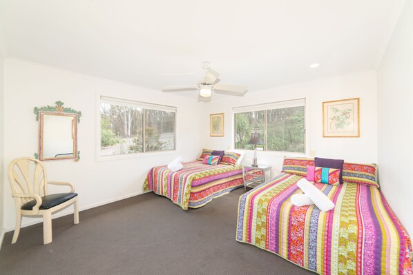A room with two beds, a chair, and large windows.