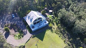 An aerial view of a house with a large deck, surrounded by dense forest.