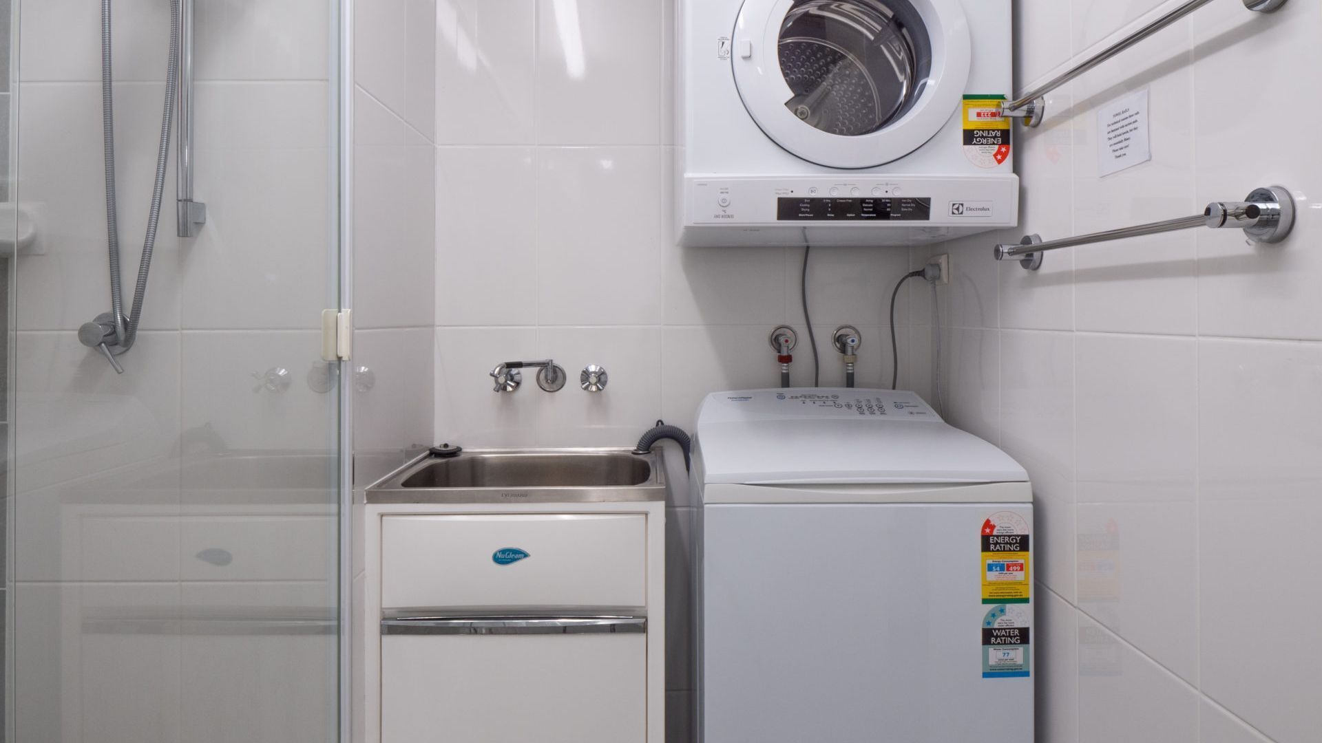 Ein kleines Badezimmer mit Duschkabine aus Glas, integriertem Waschmaschine und kleinem Waschbecken.