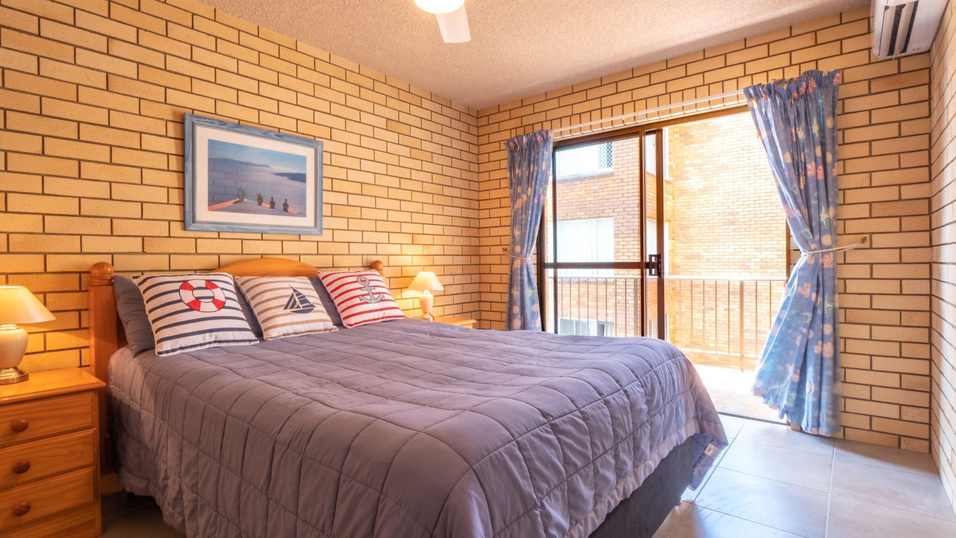 Une chambre à coucher avec un lit, une table de chevet, un tiroir, une fenêtre avec des rideaux et un tableau au mur.