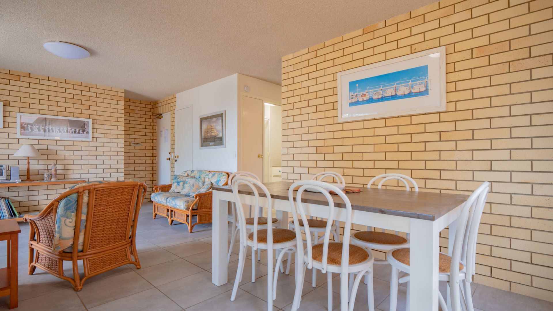 A dining area with a brick wall, white chairs, and a wooden table.