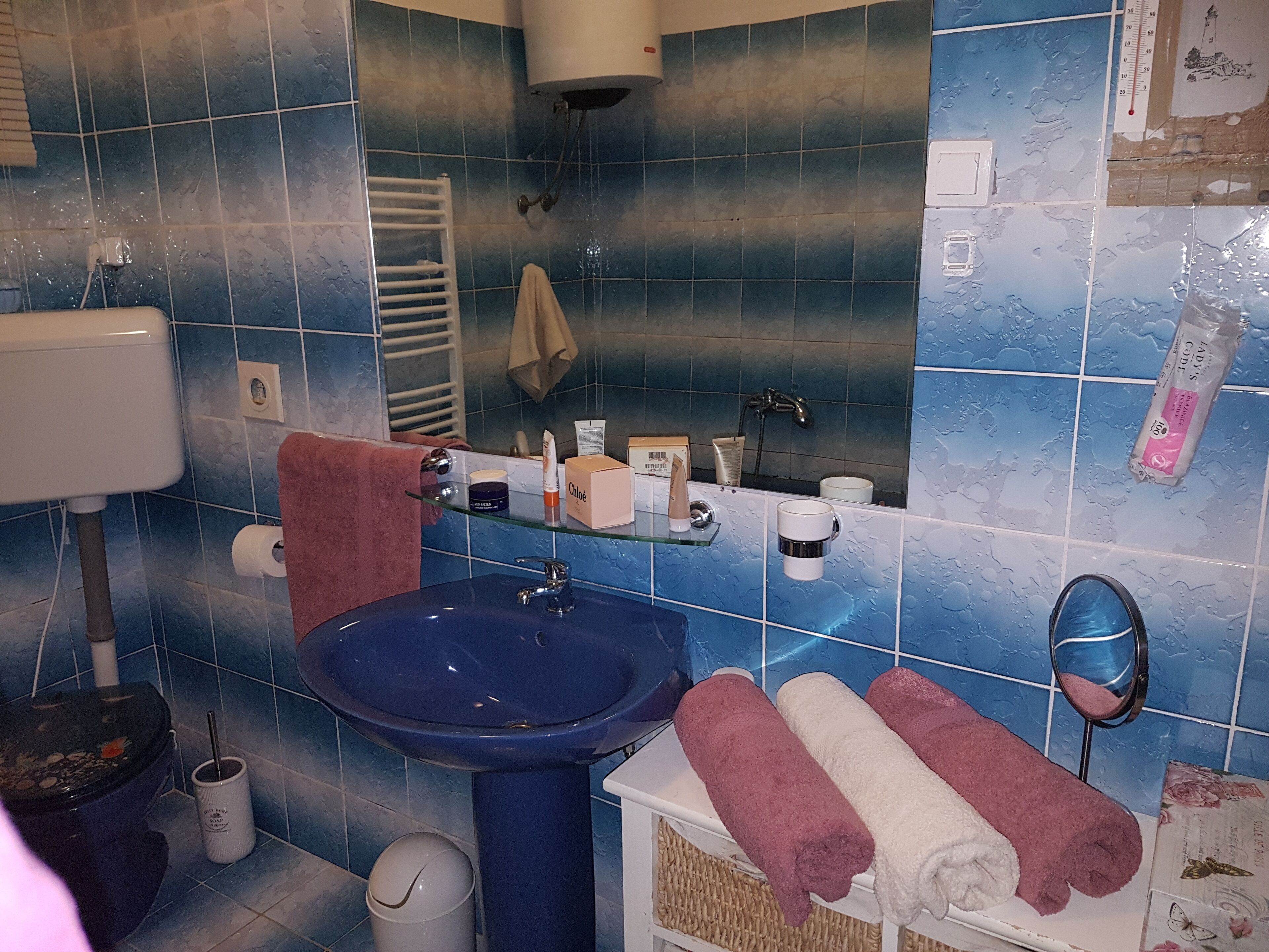 Une salle de bain avec un lavabo bleu, des toilettes, un miroir et un porte-serviettes.