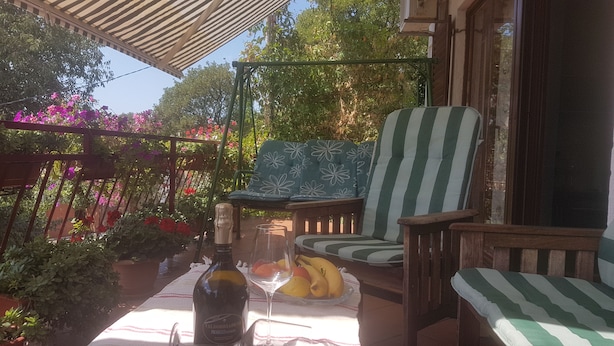 Een terras met een tafel, stoelen, een fles wijn en fruit.