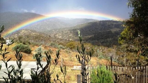 Paisatge amb un arc de sant martí sobre una vall, una tanca de fusta i vegetació al primer terme.