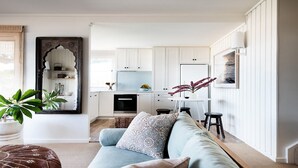 A modern living room with a sofa, a coffee table, and a kitchen area with white cabinets and a black stove.