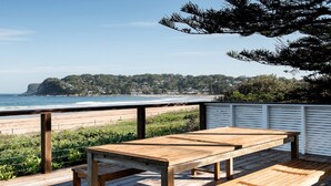 A wooden deck with a table and benches overlooking a beach and ocean.