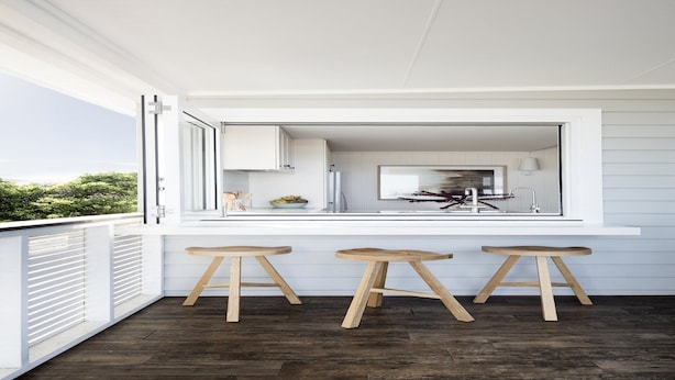 A modern kitchen with a large window, wooden stools, and a view of the outdoors.