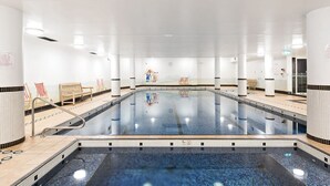 Une grande piscine intérieure à l’eau claire, entourée de murs blancs et de sols carrelés.