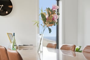 A dining table with chairs, a vase with flowers, and a clock on the wall.