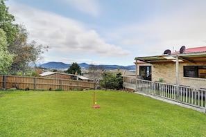A backyard with a grassy lawn, a wooden fence, and a house with a satellite dish. - Large house, centrally located with amazing views  (Lenah Valley)