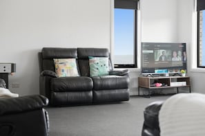 A modern living room with a leather sofa, a flat-screen TV, and a bookshelf.