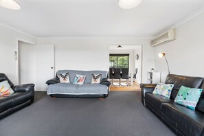 A modern living room with two black leather sofas, a grey sofa with patterned cushions, and a black floor lamp.