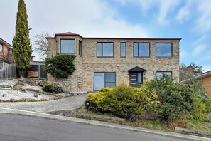 A two-story stone building with a red roof, a front door, and multiple windows.