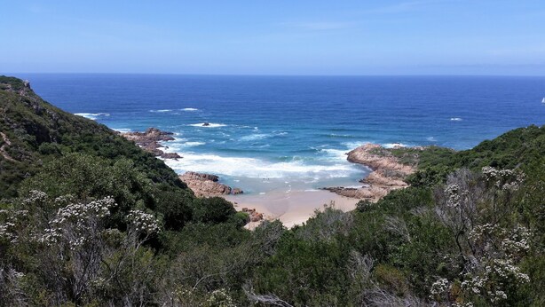 Paisaje costero con acantilados rocosos, una playa de arena y abundante vegetación.