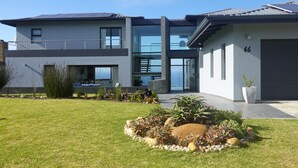Una casa moderna de dos pisos con garaje, césped cuidado y diversas plantas.