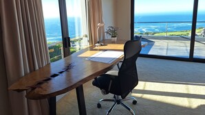 Una habitación con escritorio, silla y ventanas amplias que dan al océano.
