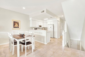 A modern kitchen with white cabinetry, a central island, and a dining area with white chairs and a wooden table.