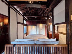 Una habitación tradicional japonesa con suelo de tatami, techo de madera bajo y una cama con ropa de cama blanca.